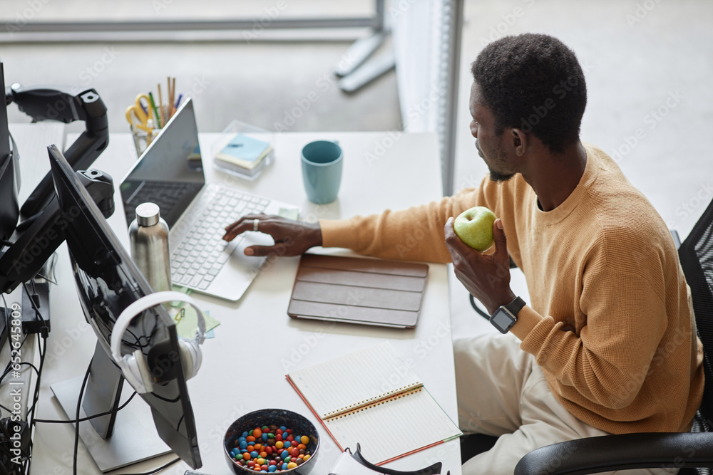 Wall mural high angle view of programmer eating green apple and working on laptop in it office