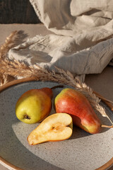 Ripe red and yellow whole and half pear on plate, linen tablecloth, dried meadow grass on beige...