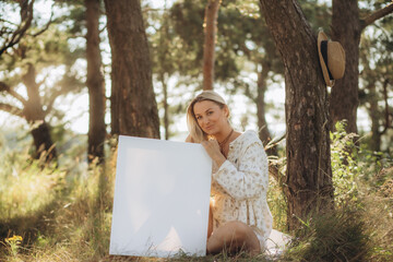 Fototapeta na wymiar girl artist, woman paints picture landscape, summer forest, denim shorts, creating creativity artistic mood. Blank white canvas getting started. Grass trees background.