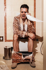 Rich man, dressed in a radiant golden suit, sits on a toilet and cries