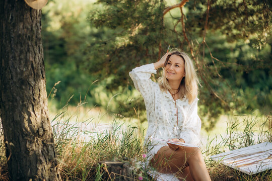 a middle-aged female artist paints a picture in nature.