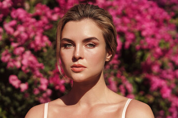 Beautiful blonde woman with smooth skin and natural makeup, as she poses against a backdrop of a bush with delicate pink flowers © blackday