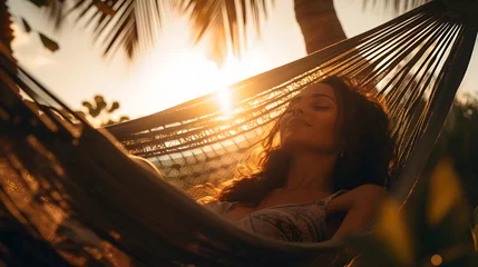 Photo sur Plexiglas Coucher de soleil sur la plage Beautiful woman lying in a hammock in between palm trees on tropical beach at sunset