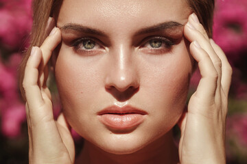 Fototapeta premium Beautiful blonde woman with smooth skin and natural makeup, as she poses against a backdrop of a bush with delicate pink flowers