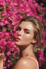 Naklejka premium Beautiful blonde woman with smooth skin and natural makeup, as she poses against a backdrop of a bush with delicate pink flowers