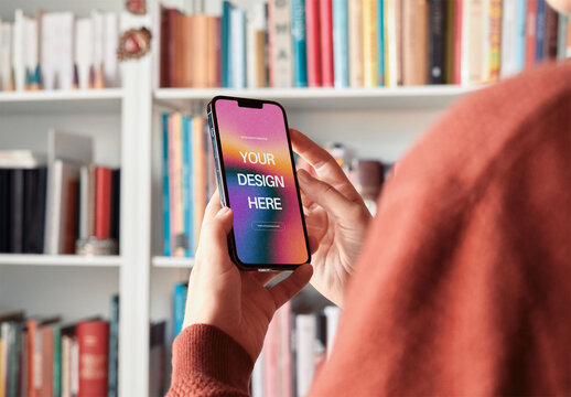Mockup of woman using smartphone with customizable screen by book shelf