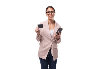 young caucasian woman with black hair gathered in a ponytail dressed in a beige jacket holds a...