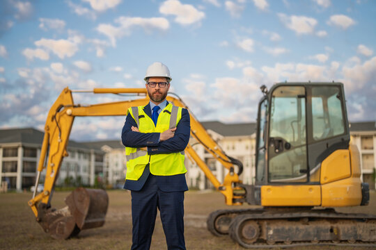 Construction builder manager or supervisor at a construction site. Portrait of construction manager worker in hardhat and suit near excavator. Renovation with construction manager or supervisor.