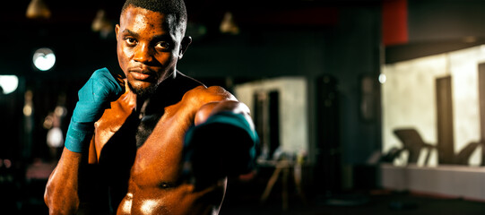Fototapeta na wymiar Boxing fighter shirtless posing, african boxer punch his fist in front of camera in aggressive stance and ready to fight at gym with kicking bag and boxing equipment in background. Spur