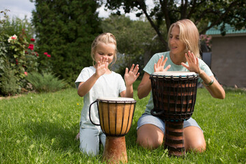 mom and child daughter play at ethnic drums sitting on the grass on a sunny day. a family hobby....