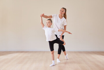 Fototapeta premium Beautiful woman teacher and a little girl perform dance movements in a bright studio. The concept of education, dance, sports, Pilates, stretching, healthy lifestyle.