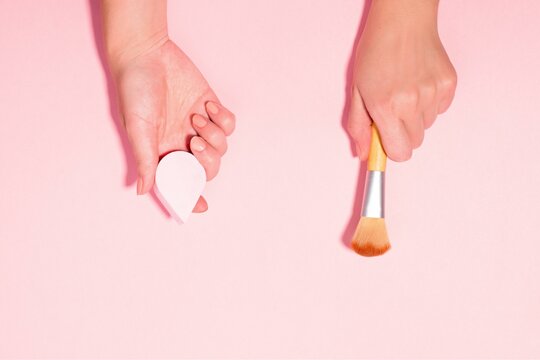 Female Hands Holding Beauty Blender and Brush on Pink Background