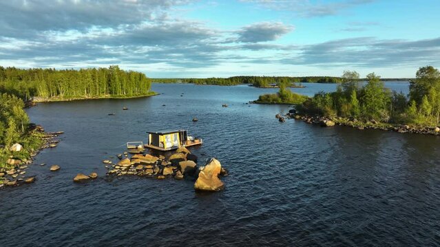 Aerial pull back away from a bathhouse hut, on a rocky isle in sunny Finland
