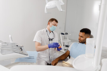 Obraz premium Closeup to the camera good looking dentist with protective mask explains the process of fixing the braces to teeth he using the tooth model for this