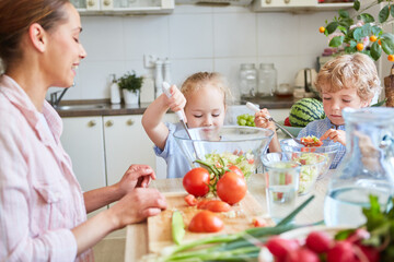 Mother teaching kids to prepare salad at home