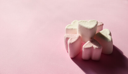 Delicate pink and white marshmallows in the shape of a heart on a pink background with copy space, banner. Marshmallow sweets closeup on a light background. Valentine's Day symbols tender marshmallow.