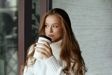 Beautiful woman drinking coffee. Girl holds paper cup of hot coffee