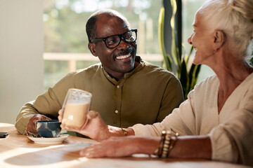 Happy senior couple sitting at table and talking to each other for cup of coffee in cafe