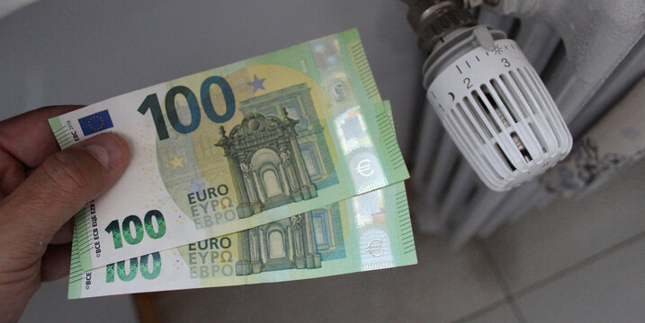 Banconote da 100 euro nelle mani di un uomo e valvola termostatica per calorifero con riscaldamento centralizzato - risparmio energetico