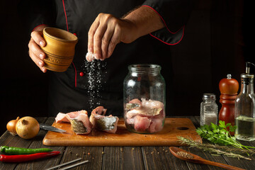 A chef salts steaks with raw fish before cooking herring in a jar. Concept of salting or canning...