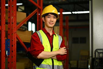 Portrait of confident male warehouse worker wearing reflective jackets standing with arms crossed and looking at camera
