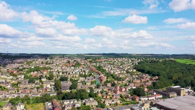 Aerial footage of the town of Batley in the UK, showing the housing estates on a sunny day in the summer with white clouds in the sky