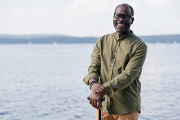 Portrait of African American happy senior man smiling at camera while walking near the lake - Powered by Adobe
