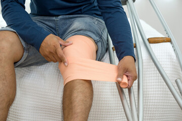 A man with a broken knee sitting on his bed. He leans on crutches, signalling recovery from injury....