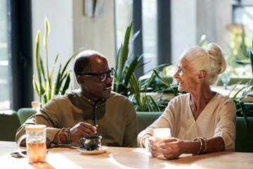 Happy senior couple drinking coffee and talking to each other while having date in cafe