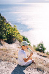 Naklejka na ściany i meble child on a cliff overlooking the sea drinks water, travel and active lifestyle