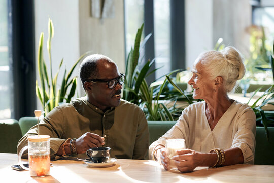 Happy senior couple drinking coffee and talking to each other while having date in cafe