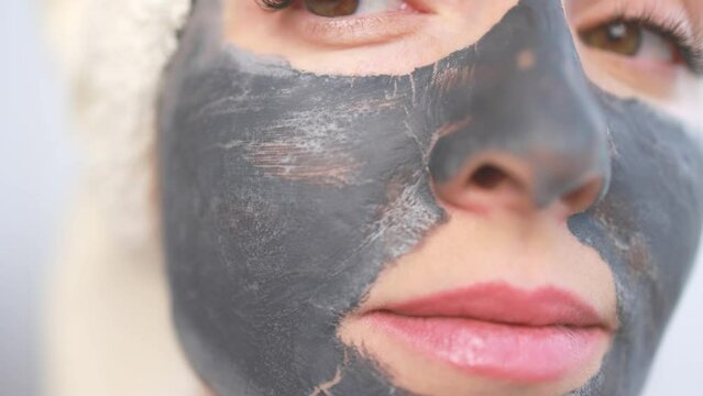 A woman applies a cleansing mask to her face.