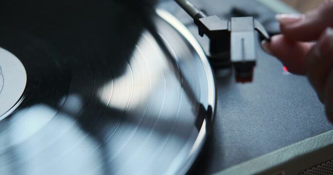 Delicate female hands skillfully operate a vintage vinyl record player. The tactile moment of starting the player evokes nostalgia and a deep appreciation for the analog world of music.