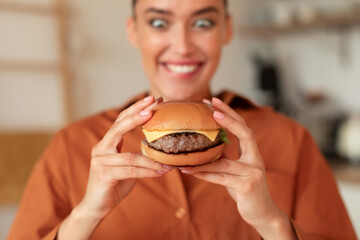 Fast food addiction. Portrait of hungry woman holding burger and looking at it with wide open eyes, selective focus - obrazy, fototapety, plakaty