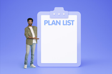 Happy young indian guy in casual point hand on plan list with empty space