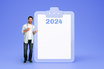 Smiling young european man in casual point fingers on plan for 2024 year with free space, recommended time management