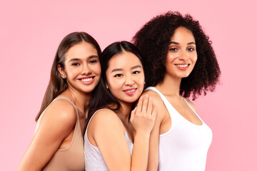 Positive young international women friends posing and smiling at camera isolated on pink...