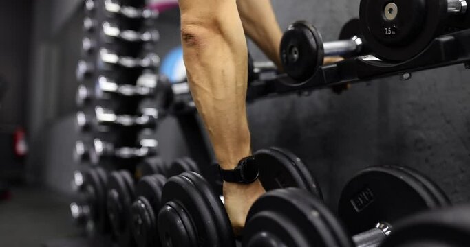 Man hand takes dumbbells for bodybuilding in gym. Closeup of man's hands lifting weights in sports club