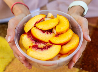 Outdoor close up of hands handling food. Woman hand holding peach or nectarine slices. Picnic concept
