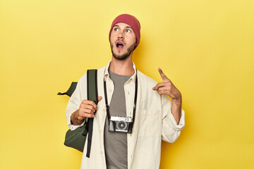 Man with vintage camera and backpack on yellow pointing to the side