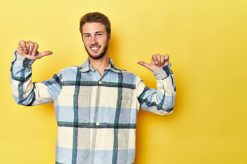 Young Caucasian man on a yellow studio background feels proud and self confident, example to follow.