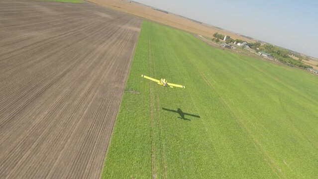 FPV Drone View of Small Crop Duster Plane Skimming Low Over Rural Grass Runway