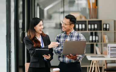 Asian business colleague business presents and explains and using laptop and tablet. Teamwork, financial marketing team, while sitting in modern office
