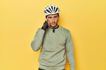 Casual dressed Latino cyclist on yellow pointing temple with finger, thinking, focused on a task.