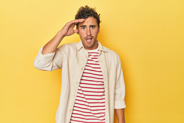 Young Latino man posing on yellow background shouts loud, keeps eyes opened and hands tense.