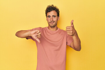 Young Latino man posing on yellow background showing thumbs up and thumbs down, difficult choose concept