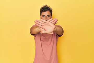 Young Latino man posing on yellow background doing a denial gesture