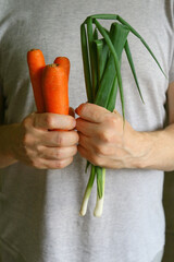 Man holds green onions and carrots in his hands, close-up. Fresh vegetables. Vertical photo.