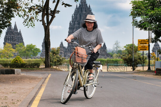 Asian woman riding rental bicycle with Prambanan temple at the background