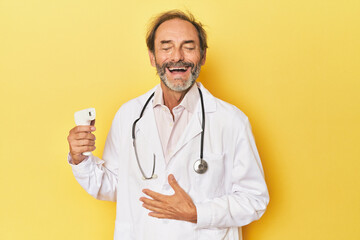 Doctor holding infrared thermometer in studio laughs out loudly keeping hand on chest.